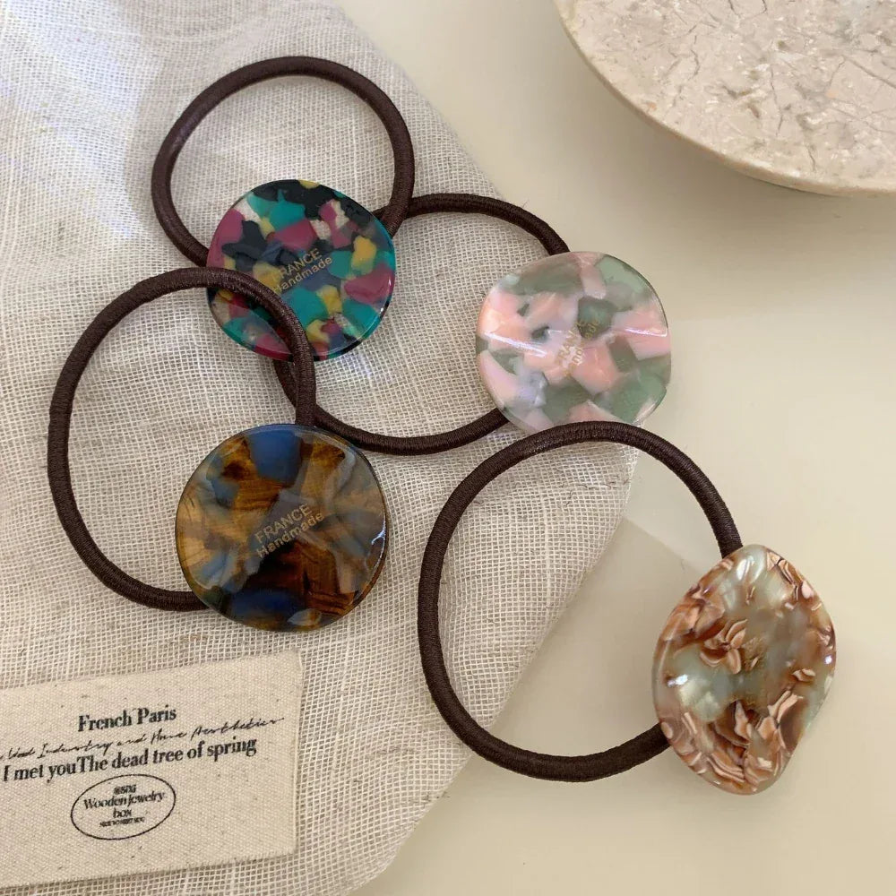 Five marbled round charm hair ties displayed on a beige cloth
