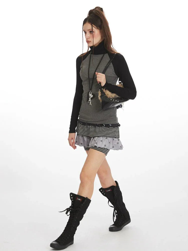 Model walking in a gray and black long-sleeve turtleneck top with a layered skirt and black boots.