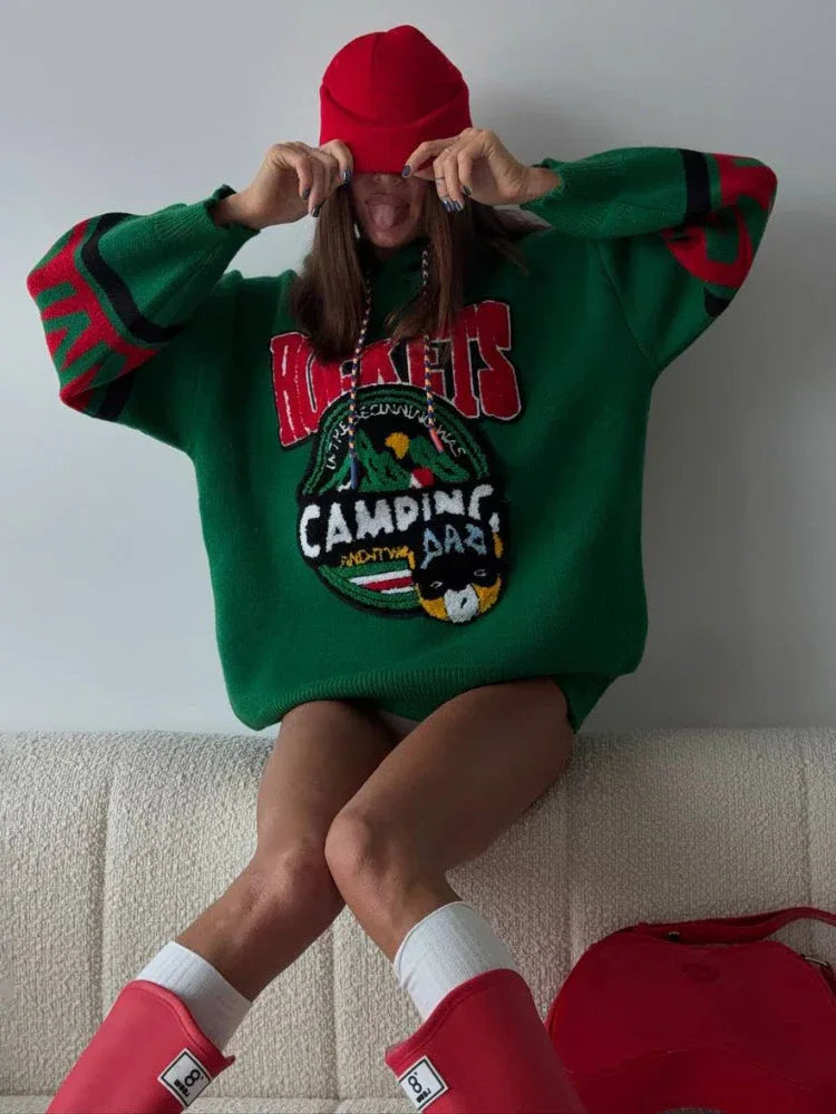 Woman wearing an oversized green knit hoodie with a red beanie and red boots, sitting on a couch
