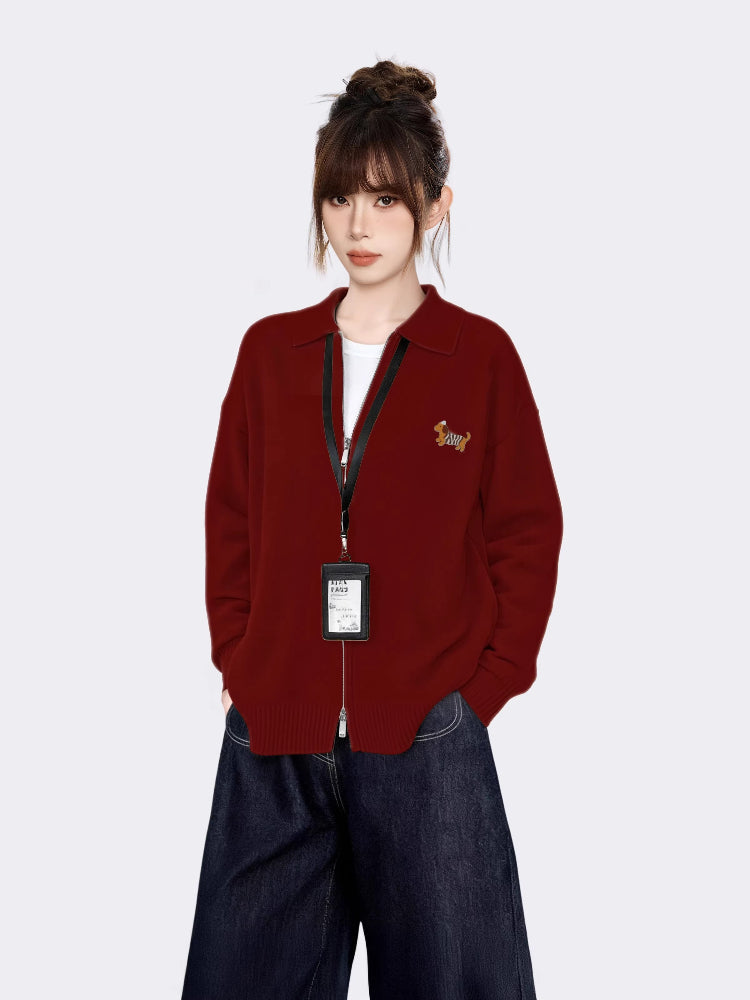 Woman wearing a maroon zip-up knit cardigan with a small embroidered tiger graphic on the left chest, a white t-shirt underneath, and dark wash wide-leg jeans.