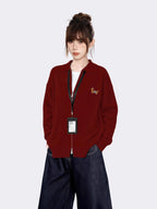 Woman wearing a maroon zip-up knit cardigan with a small embroidered tiger graphic on the left chest, a white t-shirt underneath, and dark wash wide-leg jeans.