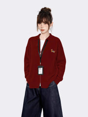Woman wearing a maroon zip-up knit cardigan with a small embroidered tiger graphic on the left chest, a white t-shirt underneath, and dark wash wide-leg jeans.