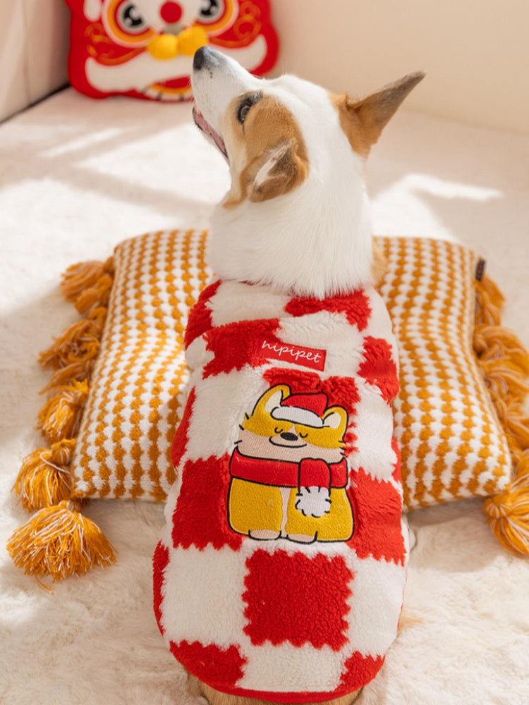 Rear view of a corgi dog wearing a red and white checkered plush sweater with a cartoon embroidery of a dog in a Santa hat, resting on a pillow.