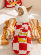 Rear view of a corgi dog wearing a red and white checkered plush sweater with a cartoon embroidery of a dog in a Santa hat, resting on a pillow.