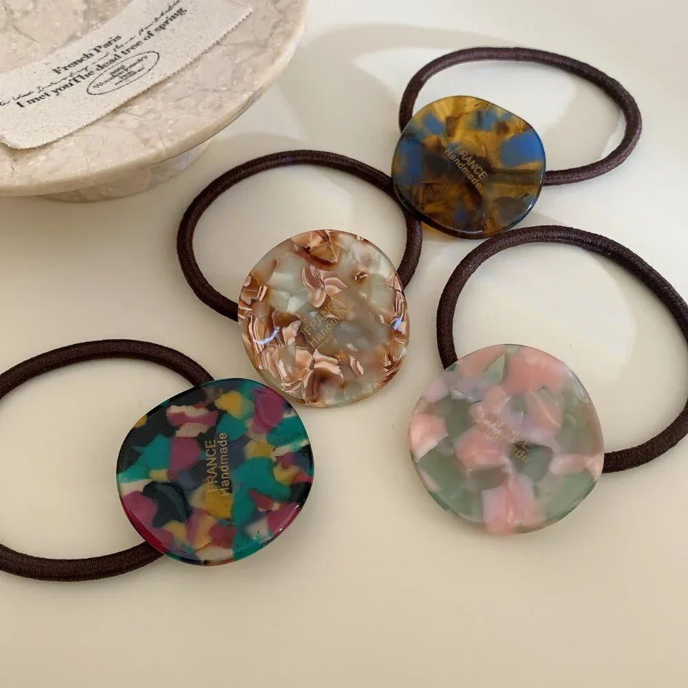 Five marbled round charm hair ties scattered on a white surface
