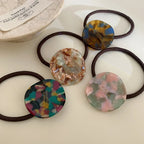 Five marbled round charm hair ties scattered on a white surface