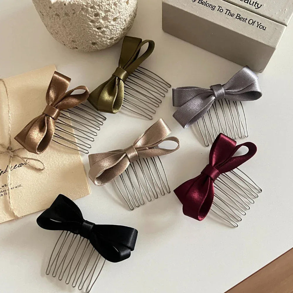 A collection of satin bow hair combs in various colors including champagne, olive green, gray, burgundy, and black, arranged on a white surface.