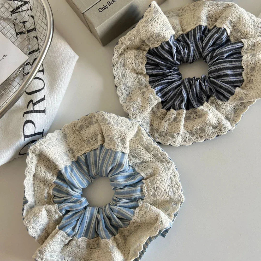 Two scrunchies on a white surface, one with blue and white stripes and the other with dark blue and white stripes, both with lace trim.