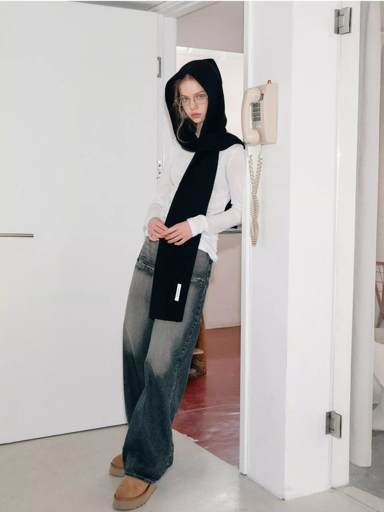 Woman wearing a black hooded scarf with a large bow detail, standing in a doorway.