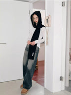 Woman wearing a black hooded scarf with a large bow detail, standing in a doorway.