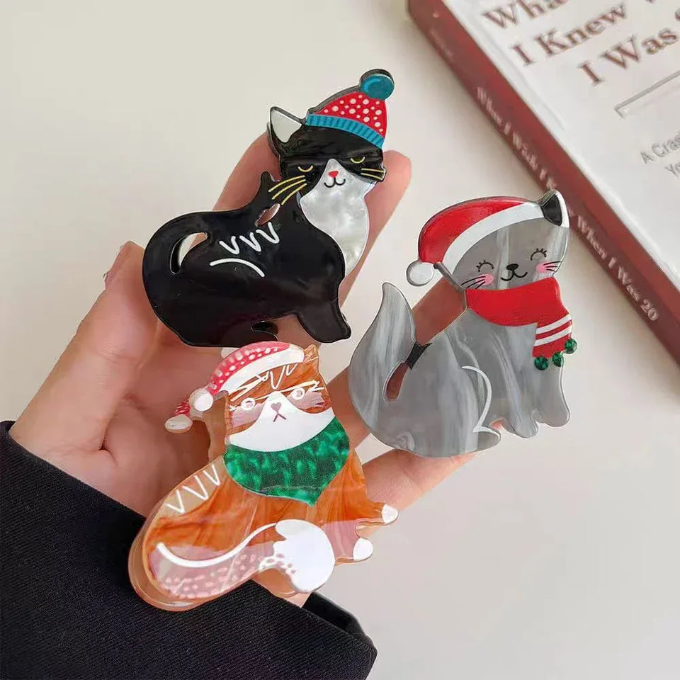 Three acrylic cat brooches in a hand, featuring holiday designs. Secondary image