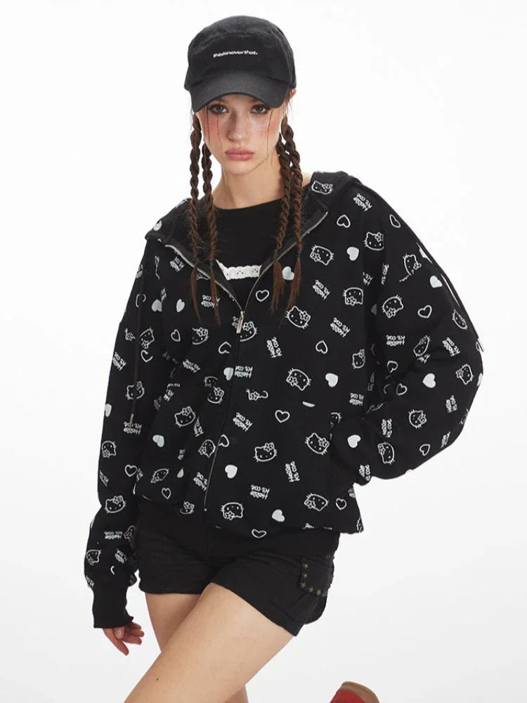 Front view of a model wearing a black zip-up hoodie with an all-over white Hello Kitty and heart graphic print, black t-shirt, black shorts, black knee-high socks, and red sneakers. The model is wearing a black baseball cap and has her hair in braids, with the zipper partially open.