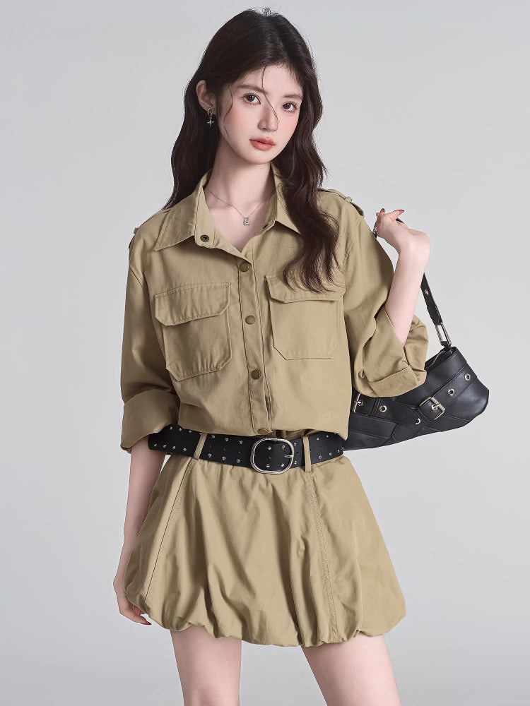 Woman wearing a tan button-down shirt dress with a black studded belt and a black shoulder bag.