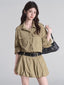 Woman wearing a tan button-down shirt dress with a black studded belt and a black shoulder bag.