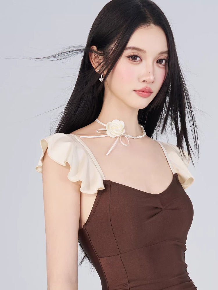 Close-up of the brown and cream one-piece swimsuit, highlighting the ruffled cap sleeves and pearl necklace.
