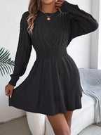 Woman wearing a black long-sleeved knit dress with cable knit detailing on the bodice, adjusting the skirt.