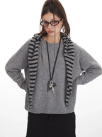 Woman wearing a grey knit sweater with a striped scarf, black cargo pants, and glasses, with her hands on her hips.