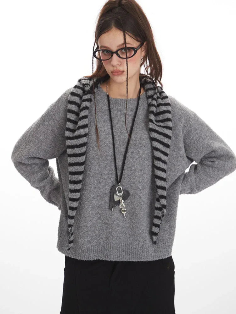 Woman wearing a grey knit sweater with a striped scarf, black cargo pants, and glasses, with her hands on her hips.