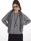 Woman wearing a grey knit sweater with a striped scarf, black cargo pants, and glasses, with her hands on her hips.