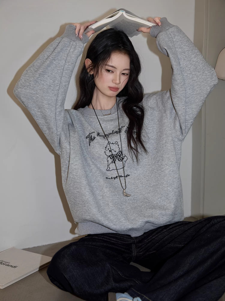 Woman wearing a grey crew neck sweatshirt with a graphic print of a bear wearing a checkered scarf