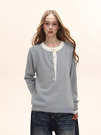 Woman wearing a light grey knit henley sweater with a white collar and dark wash wide-leg jeans.