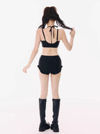Back view of a model wearing a black bikini top, black ruffled shorts, and black platform boots.
