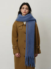 Woman wearing a blue scarf and a brown coat, with her hands in her pockets