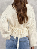 Back view of a woman wearing a cream chunky knit wrap sweater tied at the waist with light wash jeans.