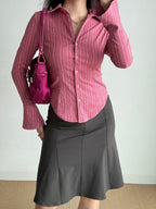 A woman wearing a pink striped shirt, a charcoal skirt, and holding a pink handbag.