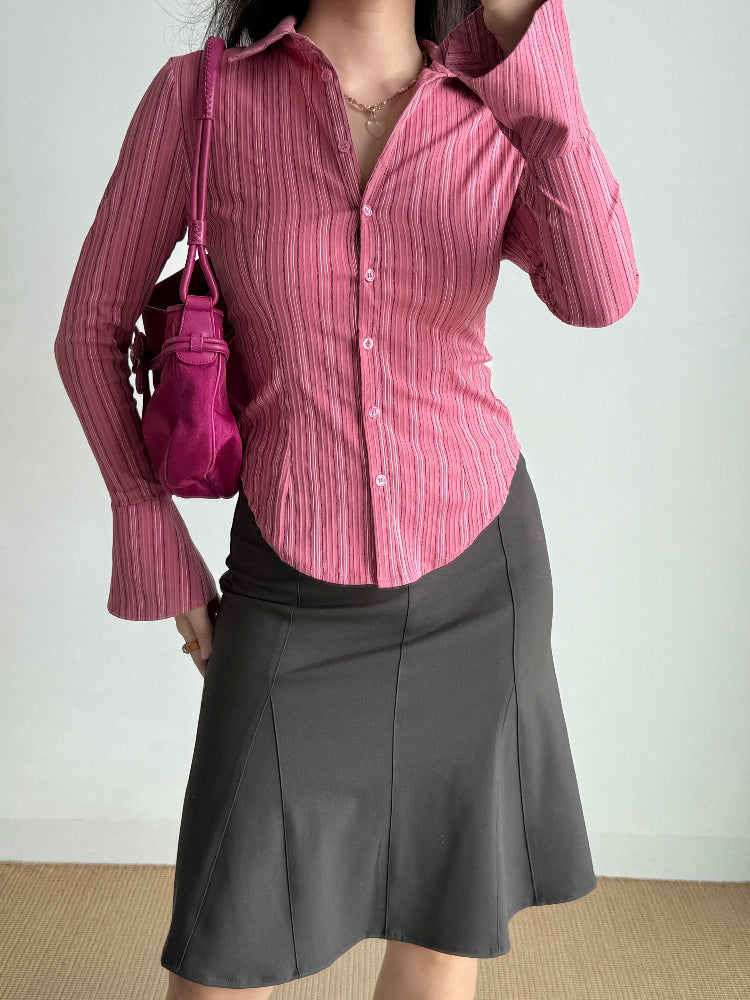 A woman wearing a pink striped shirt, a charcoal skirt, and holding a pink handbag.