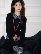 Close-up of a model's upper body wearing a black long-sleeved top with a checkered collar and cuffs, and a small brown pendant necklace.