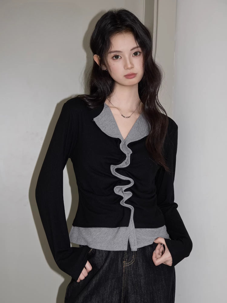 Woman wearing a black long-sleeved top with grey ruffled trim and dark wash wide-leg jeans.