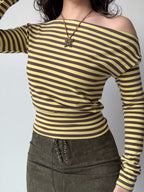Woman in a yellow and brown striped off-the-shoulder long-sleeve top and a brown lace-up mini skirt, showing off the outfit's styling.