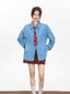 Model wearing an oversized blue collared shirt with a red plaid tie and a red plaid mini skirt, standing with hands on hips.