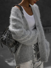 Model wearing a light grey fuzzy V-neck button-up cardigan over a white tank top, paired with silver metallic pants and a metallic handbag.