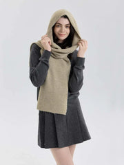Model wearing a gray sweater and pleated skirt with a beige hooded scarf wrapped around her neck and hood up.