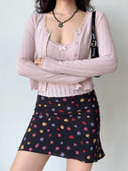 Woman wearing a pink cropped knit cardigan with lace trim and a floral print skirt.