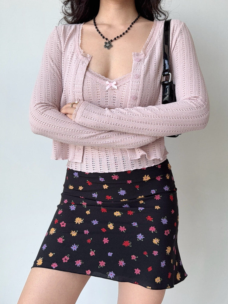 Woman wearing a pink cropped knit cardigan with lace trim and a floral print skirt.