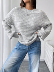 Woman posing with hands on hips wearing a light grey oversized knit sweater with balloon sleeves and a crew neck, paired with blue denim jeans.