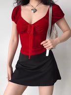 A person wearing a red velvet tie-front top and a black skirt, holding a silver purse.