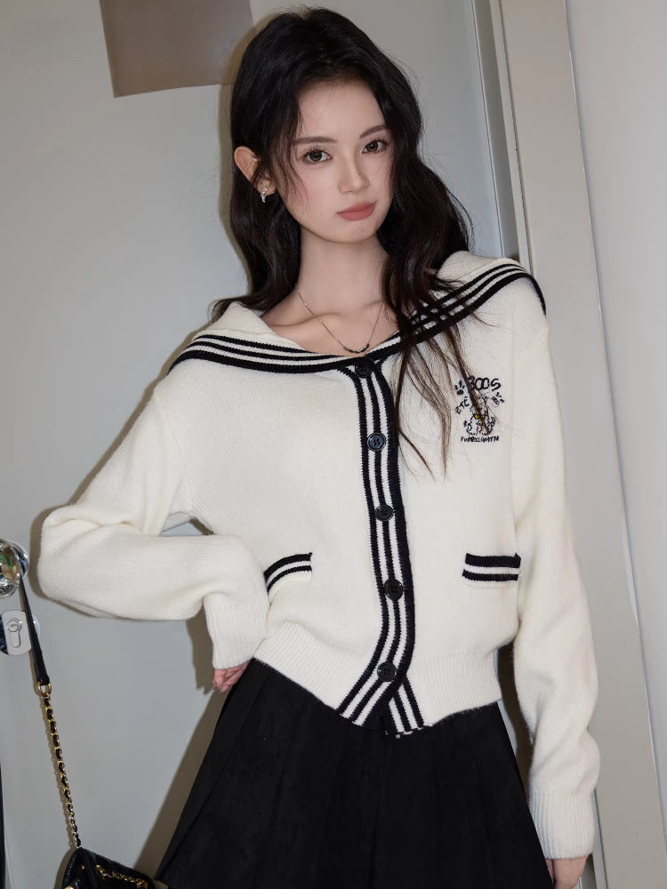 Woman wearing a white knit cardigan with black trim and a sailor collar, paired with a black skirt.