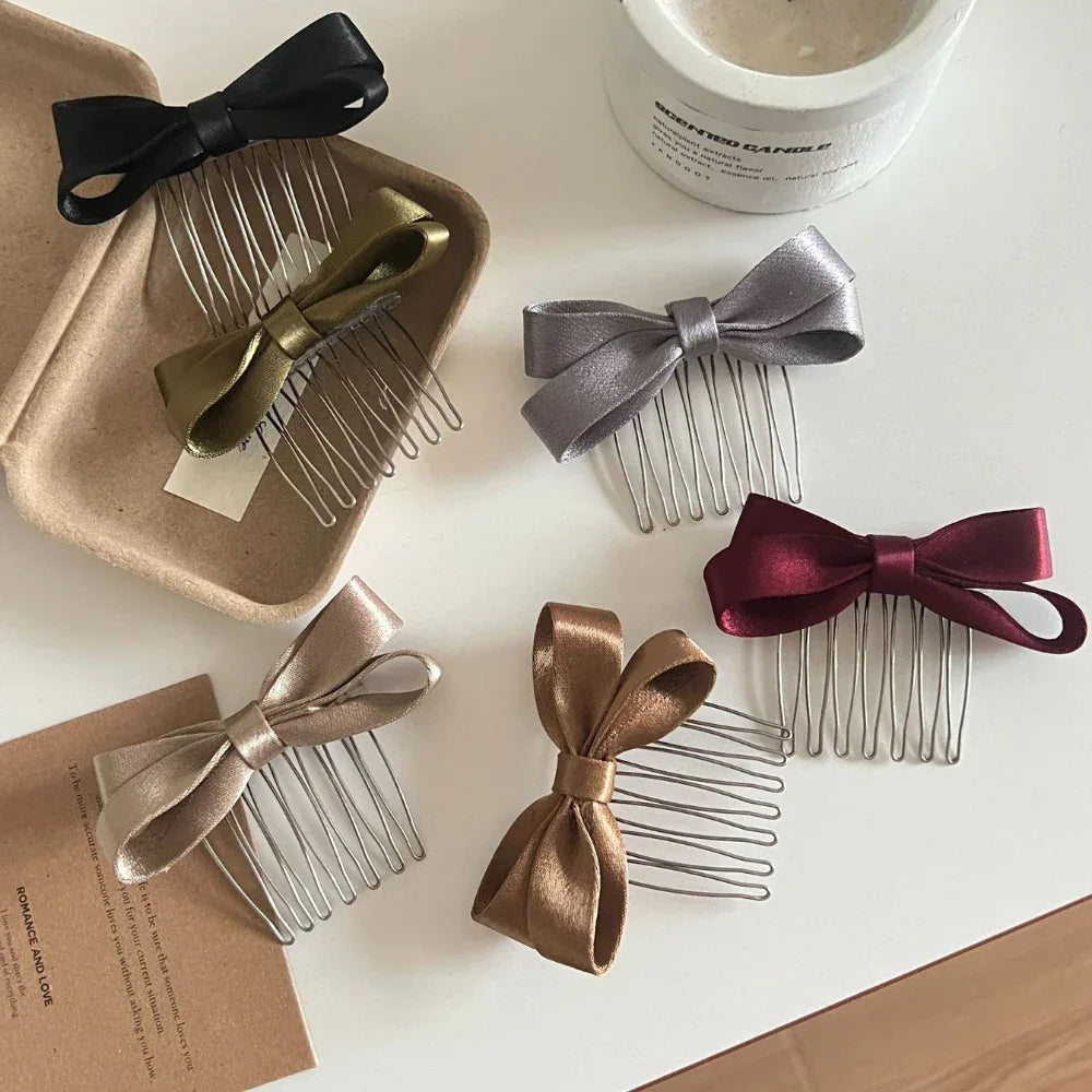 A variety of satin bow hair combs are showcased on a white surface, some placed in a brown tray.
