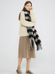 Full body shot of a woman wearing a cream cable knit sweater, a beige skirt, and a black and beige plaid scarf with fringe.