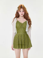 Model wearing a green floral print one-piece swimsuit with built-in shorts and a sheer white cardigan.