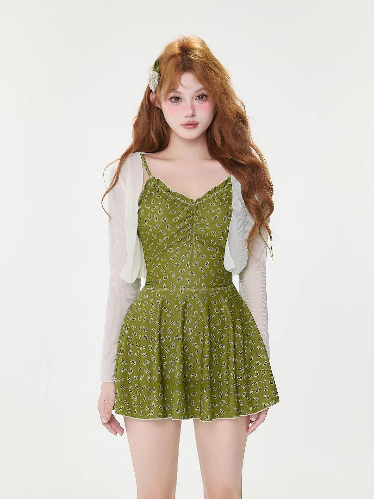 Model wearing a green floral print one-piece swimsuit with built-in shorts and a sheer white cardigan.