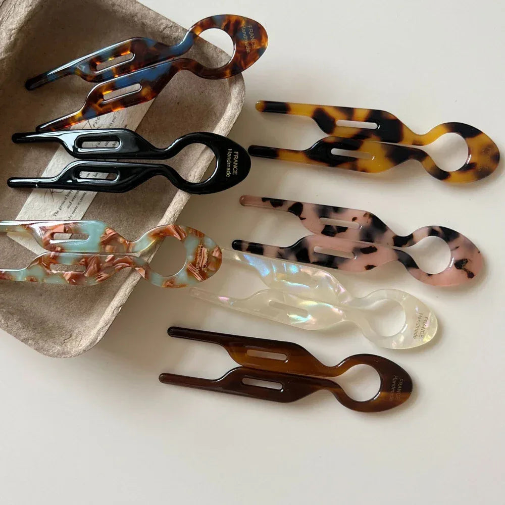 Group of resin tweezers in a variety of patterns and colors, some placed in a cardboard tray and others on a white surface.