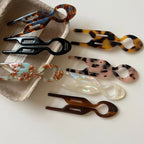 Group of resin tweezers in a variety of patterns and colors, some placed in a cardboard tray and others on a white surface.