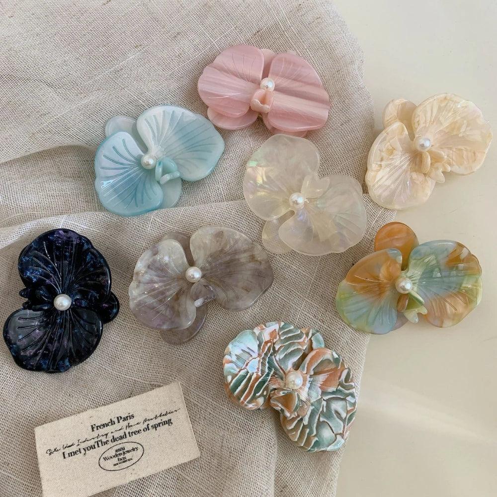 Various orchid-shaped hair clips with pearl accents displayed on fabric.