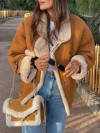 Woman wearing a brown suede jacket with white shearling trim and collar, blue jeans, and a white t-shirt, holding sunglasses and a handbag.