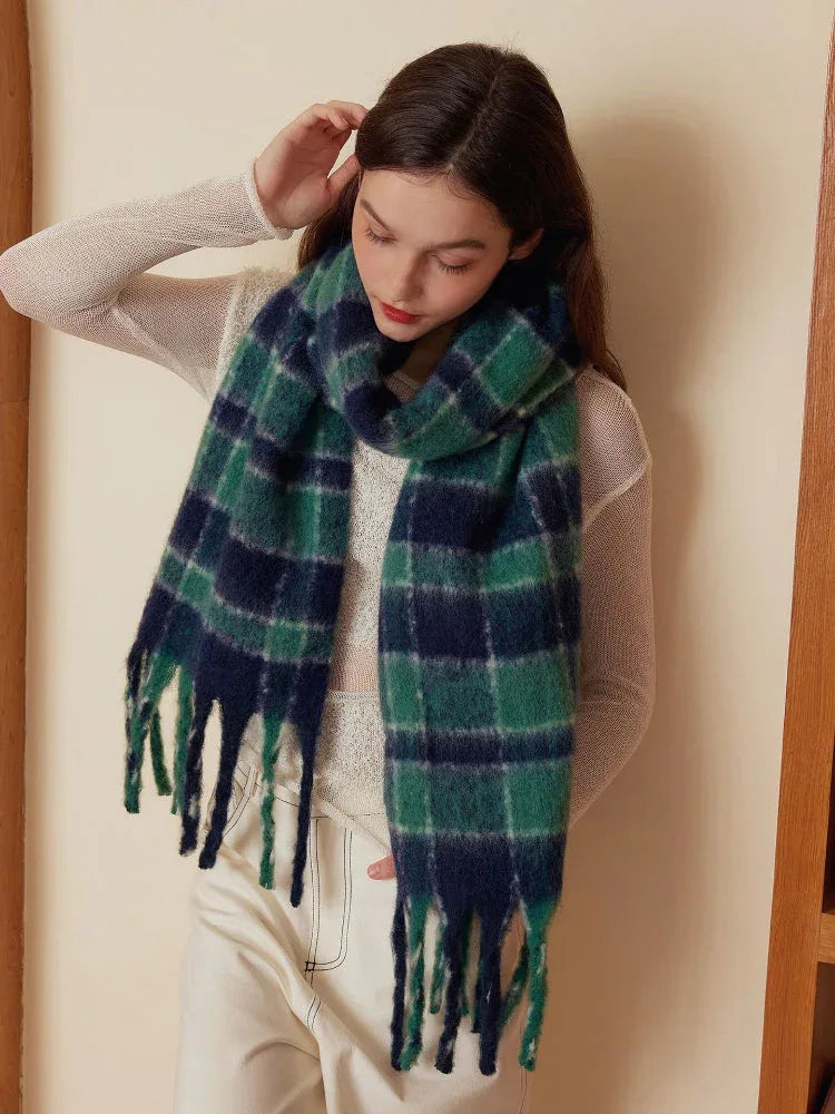 Woman wearing a green and navy plaid scarf and a white top, with her hand in her pocket.